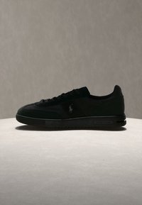 Μαύρο sneaker χαμηλής κοπής με σχέδιο κορδονιών και διακριτικό λογότυπο στο πλάι, εμφανίζεται σε φωτεινή επιφάνεια πάνω σε απλό φόντο.