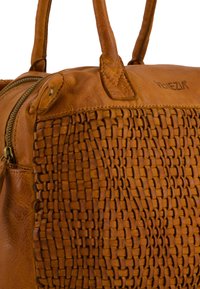 Sac à main en cuir brun avec un détail tissé sur un côté, des poignées robustes et une fermeture éclair. Texture lisse avec des accents de coutures bien marquées.