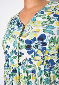 Abito a fiori in tessuto leggero, con fiori blu e gialli su sfondo bianco, scollatura a V, bottoni e vita arricciata.