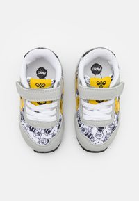 Witte sneakers met grijze suède accenten, gele details en een zwart cartoonpatroon. Klittenbandsluitingen en witte veters voor een veilige pasvorm.