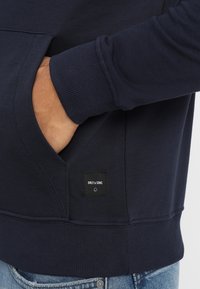 Sudadera de algodón azul marino con puños y dobladillo acanalados, con un bolsillo frontal y una etiqueta negra con la inscripción "ONLY & SONS."