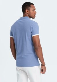 Modrá polokošile vyrobená z bavlny, s měkkou texturou, bílými akcenty na límečku a rukávech a přiléhavým střihem.