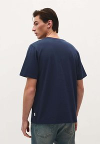 Navy blue cotton t-shirt with a crew neck and short sleeves, featuring a straight hem and small logo tag at the side. Minimal design.