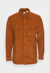 Camisa marrón de pana con cierre de botones en la parte delantera, dos bolsillos en el pecho y un cuello puntiagudo. Tela texturizada con ribete vertical.