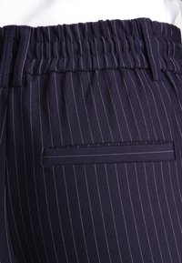 Dunkelblaue Nadelstreifen-Hose mit elastischem Bund, Gürtelschlaufen und einer horizontalen Passtasche auf der Rückseite.