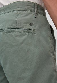 Vihreät puuvillahousut, joissa on sileä koostumus, takatasku, brodeerattu logo ja erottuva ommel vyötäröllä.