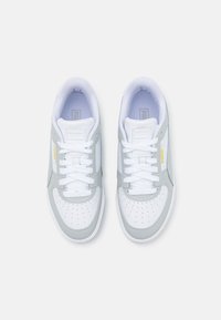 Een paar witte en lichtgrijze Puma-sneakers met witte veters en een gouden Puma-logo, gezien vanuit bovenaf tegen een witte achtergrond.