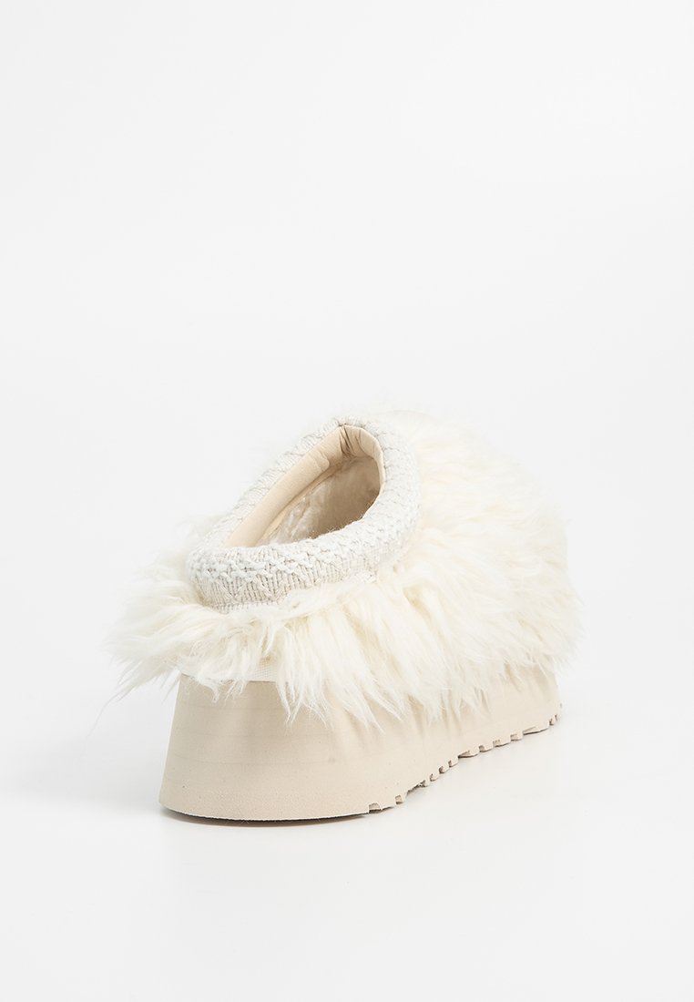 Zoccoli bianchi in pelliccia sintetica senza schienale, con un colletto in morbido tessuto e una suola liscia color beige, caratterizzati da una leggera piattaforma e una forma curva.