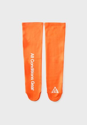 Para jasnych pomarańczowych rękawów na ramiona, jeden z napisem "All Conditions Gear", drugi z trójkątnym logo zawierającym litery "ACG".