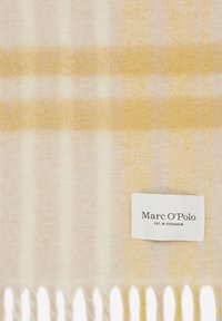 Écharpe en laine douce avec un motif à carreaux jaune pâle et crème et des bords frangés, portant une étiquette blanche Marc O’Polo.