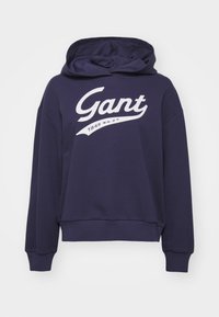 Navy blue pullover hoodie made of cotton blend, featuring a large white "Gant" logo and "1949 N.H.C.T." text in a curved design.