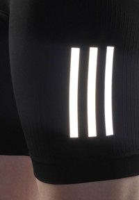 Shorts de sport noirs avec trois bandes blanches réfléchissantes sur le côté, fabriqués dans un matériau lisse et extensible avec une coupe ajustée.