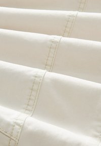 Gros plan sur un tissu couleur crème avec des coutures parallèles montrant les détails et la texture.