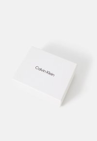 Biely obdĺžnikový box Calvin Klein s hladkým povrchom, s minimalistickým čiernym textovým logom na vrchnej straně.