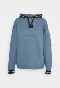 Blå bomullshoodie med en svart snörning på huvan, logotypapplikation och ribbade ärmslut. Har en ficka framtill och en något oversized passform.