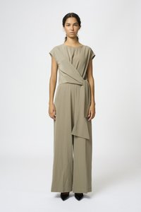 Khaki jumpsuit with short sleeves, wrap design, wide legs, and a fabric tie at the waist. Smooth texture, paired with black pointed heels.