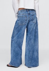 Svetlo modre široke jeans hlače iz jeansa s pobledelo teksturo. Imajo visok pas, dva zadnja žepa in neobdelane robove. Kombinirane s kratko majico.