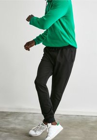 Grön hoodie med framficka, i kombination med svarta joggerbyxor och vita sneakers med gröna detaljer. Mjuk tyg och avslappnad passform.