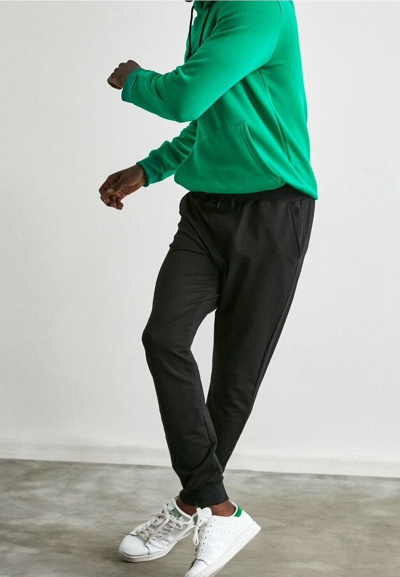 Grön hoodie med framficka, i kombination med svarta joggerbyxor och vita sneakers med gröna detaljer. Mjuk tyg och avslappnad passform.