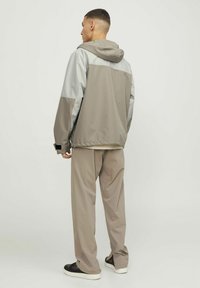 Dwukolorowa kurtka typu windbreaker w odcieniach szaro-beżowym, z kapturem, luźnym krojem i elastycznymi mankietami. Połączona z luźnymi, dopasowanymi spodniami w kolorze taupe.
