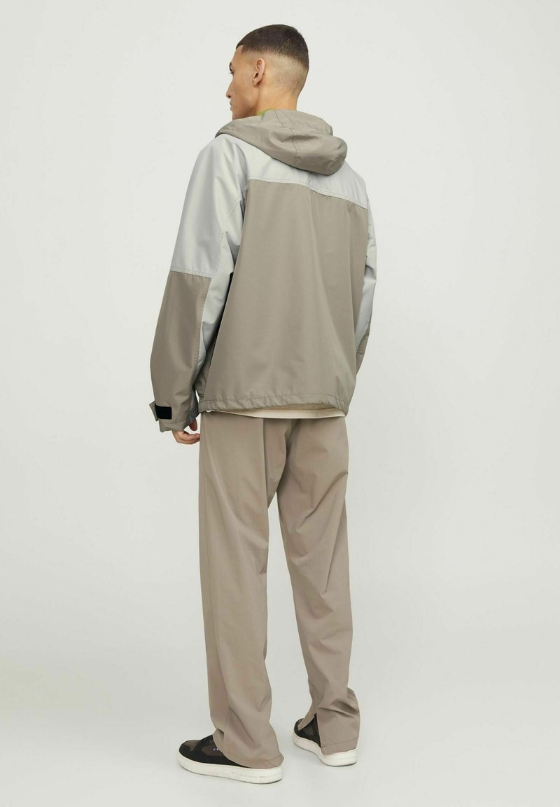 Tweedekleurige windbreakerjack in grijs en taupe, met een capuchon, een relaxte pasvorm en elastische manchetten. Gekleed met losse, bijpassende taupe broeken.