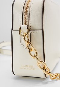 Borsa in pelle color crema con angoli, cerniera dorata, tracolla a catena e logo "Lauren Ralph Lauren" in lettere dorate.