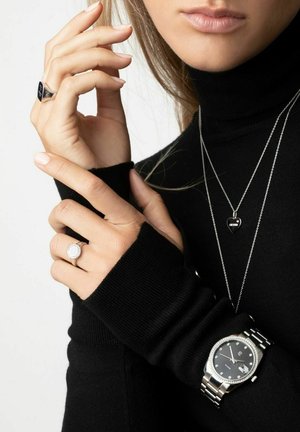 Sølvur med sort urskive og diamanter, lagd med en sølvhjertehalskæde. Modellen har en sort sweater på; viser en diamant ring.