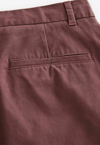 Pantalones de tela burdeos con una textura suave, un bolsillo trasero de diseño plano y costuras en contraste a lo largo de los bordes.