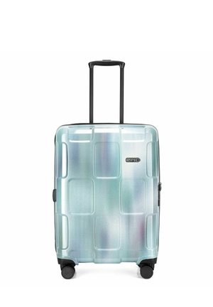 Valise rigide bleu clair avec quatre roues, une poignée télescopique noire étendue et des motifs carrés en relief sur le devant.