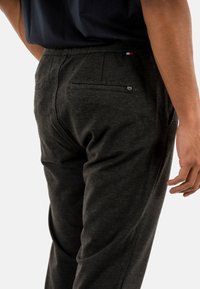 Pantaloni da uomo grigi scuri con una vestibilità comoda, realizzati in tessuto morbido. Presentano due tasche posteriori e un piccolo logo vicino alla vita.