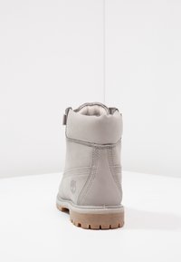 Gray suede ankle boot with padded collar, textured surface, light brown rubber sole, and a logo embossed on the heel.