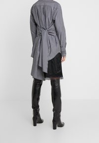 Randig skjorta i grått och vitt, knuten i ryggen med en flytande svans. Matchad med en svart satin kjol med spetskant och svarta knähöga stövlar.