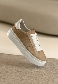 Μπεζ σουέντ αθλητικό παπούτσι με λευκά κορδόνια, με κυματιστό σχέδιο στο πάνω μέρος και χοντρή λευκή σόλα.