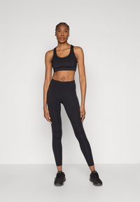 Svart sport-BH og høytsittende leggings, laget av elastisk stoff. Glatt tekstur og tettsittende design, kombinert med svarte treningssko.