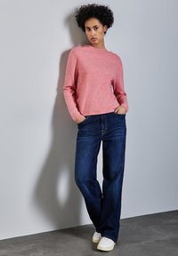 Ljusrosa stickad tröja med lång ärm, bärs med mörkblå avslappnade jeans och vita sneakers. Åtsittande, enkel design med rund halsringning.