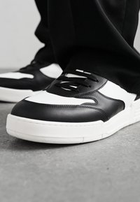 Black and white sneakers with leather upper, featuring a rounded toe, lace-up design, and textured white sole with a patterned grip.