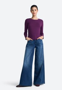 Purple ribbed long-sleeve top paired with wide-leg blue denim jeans. The top features a round neckline; jeans have a classic blue wash.