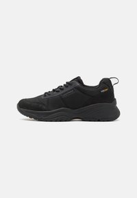 Scarpe sportive nere che presentano una combinazione di tessuto testurizzato e camoscio. Suola in gomma spessa con un motivo di battistrada; include lacci e un'etichetta di estrazione.