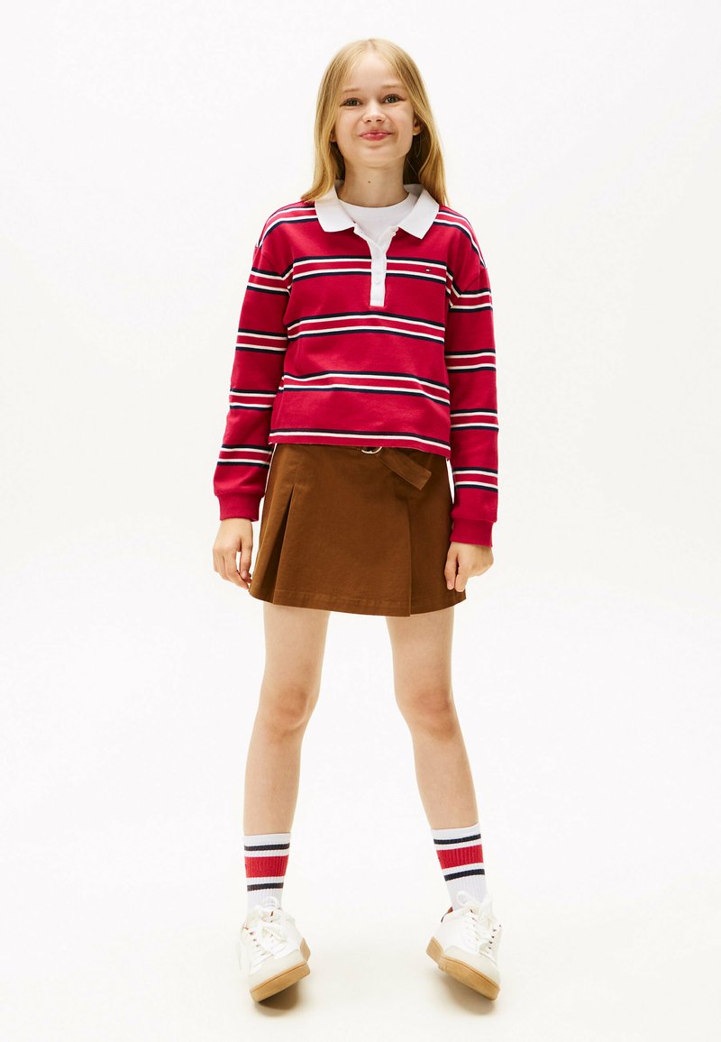 Rood-wit gestreepte lange mouwen polo shirt met een kraag, gecombineerd met een bruine plooibroek en witte sneakers met tan kleurige zolen.