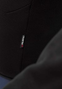 Tissu Polartec noir avec une texture lisse, arborant une petite étiquette cousue avec le nom et le logo de la marque. Design minimaliste, forme contournée.