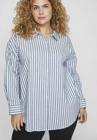 Camisa de botón a rayas azul y blanca, de manga larga y con cuello, que presenta un ajuste relajado y un dobladillo redondeado.