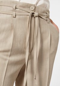 Beiga högmidjade byxor med ränder, med ett bälte med rosett och knäppning, tillverkade av texturerad tyg.
