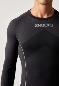 Czarna, długorękawkowa koszulka sportowa o teksturowanej powierzchni, z wyraźnym logo "SNOCKS" i kontrastowymi, białymi szwami.