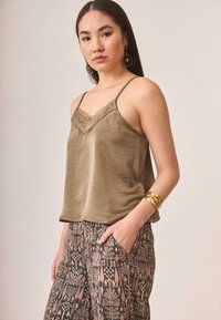 Camiseta de satén color verde oliva con puntilla y tirantes ajustables, combinada con pantalones estampados que presentan coloridos diseños florales.