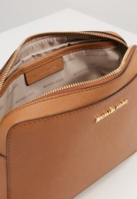 Brun tekstureret lædertaske med guldlåse og lynlås. Indvendigt har den en beige foring med gentaget brandlogo-mønster.