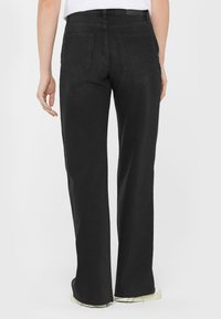 Schwarze Denim-Hosen mit entspanntem Schnitt, ausgestattet mit zwei Gesäßtaschen und einem leicht ausgefransten Saum. Glatte Textur und gerades Bein-Design.