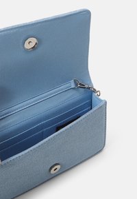 Portefeuille en tissu bleu clair ouvert montrant des emplacements pour cartes, un compartiment zippé et une fermeture pression argentée.