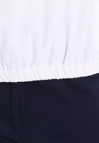 Ceinture élastique blanche d'un vêtement sur un pantalon bleu marine foncé avec des coutures visibles et le contour de la poche.