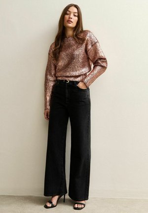 Suéter de manga corta en oro rosa con un acabado metálico texturizado, combinado con jeans de pierna ancha negros y sandalias de tacón alto negras con tiras.