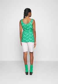 Top de tanque floral verde com cintura ajustada, calções brancos e botins verdes de salto alto. Textura suave com um padrão vibrante.